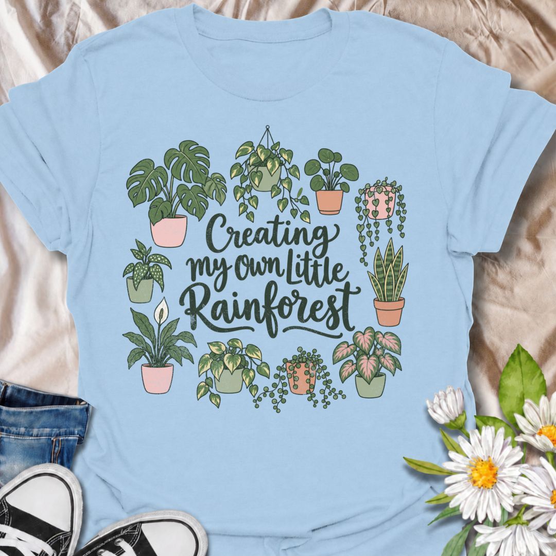 A charming houseplant T-shirt for anyone who is slowly turning their home into a lush indoor jungle. The phrase “Creating My Own Little Rainforest” is surrounded by monstera, pothos, snake plants, trailing vines, and other leafy favorites for a soft botanical design. It is perfect for plant parents, houseplant collectors, indoor gardeners, and anyone who loves filling every spare corner with greenery. The hand-drawn styling gives it a warm, feminine feel while keeping the design easy to wear. A lovely gift
