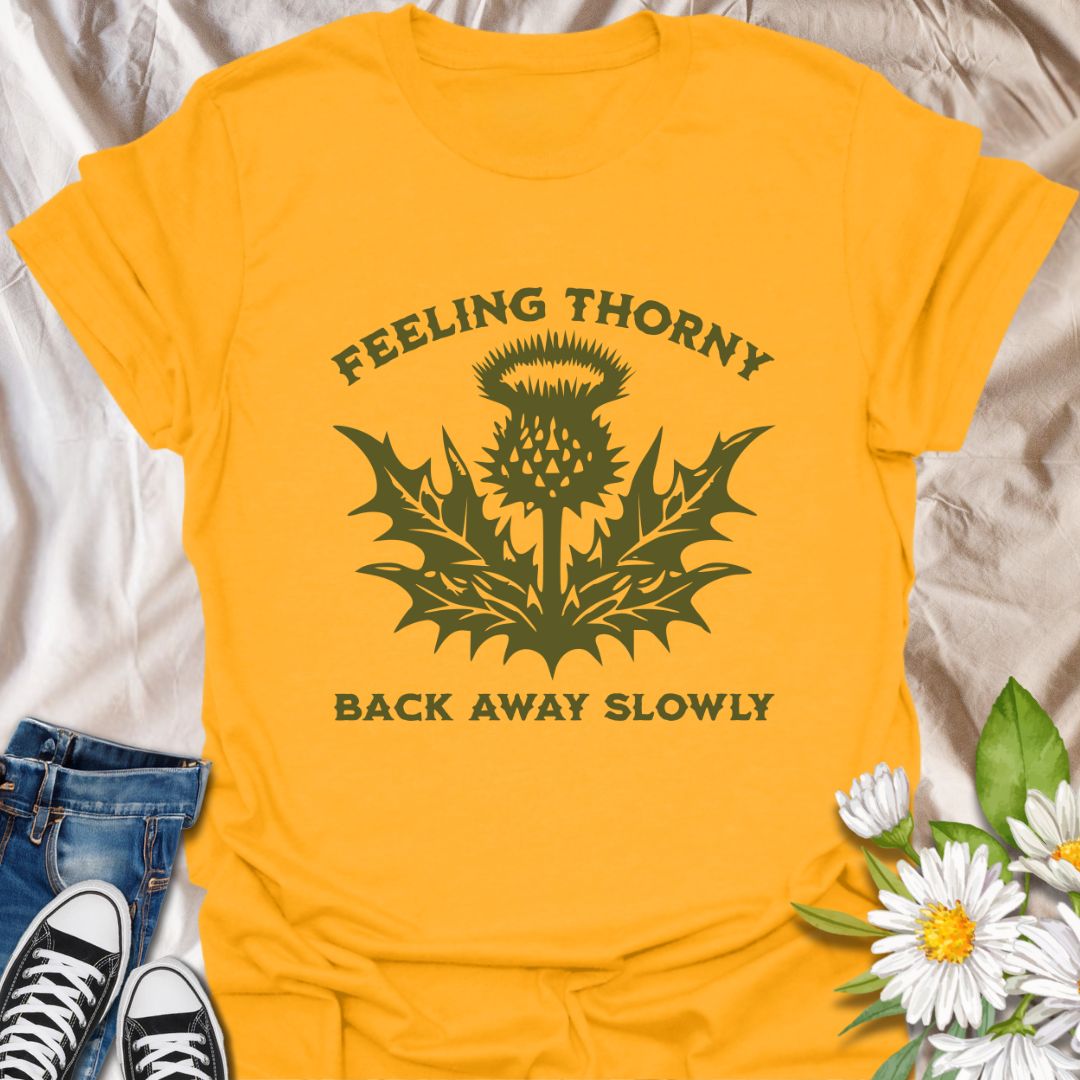 Embrace your mood with this witty “Feeling Thorny – Back Away Slowly” t-shirt featuring a bold thistle graphic. Perfect for introverts, plant lovers, and anyone with a sharp sense of humor, this quirky design makes a great gift or statement piece for everyday wear.