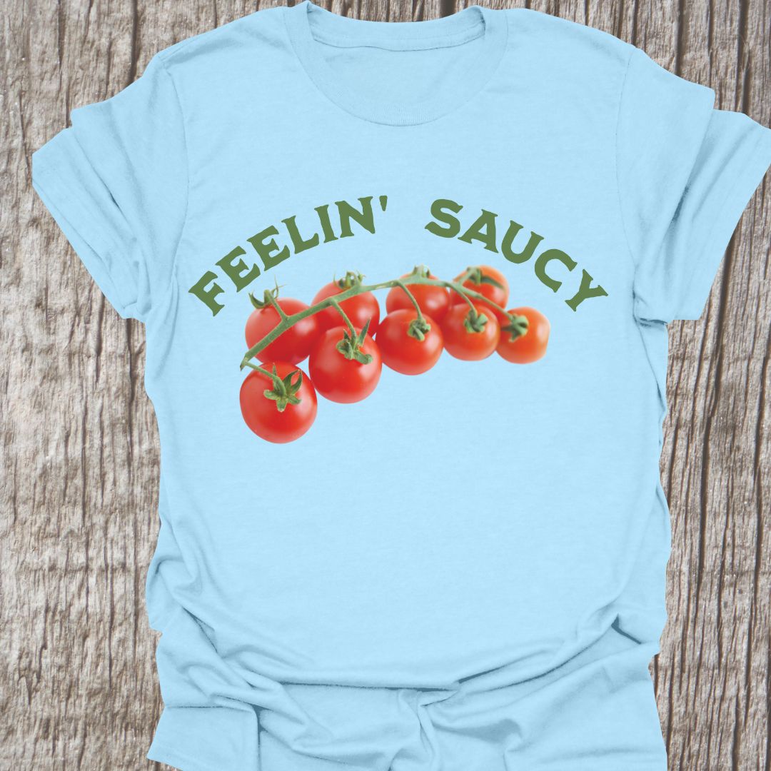 Feelin' Saucy Text written in an arch over image of tomatoes on the vine on a light blue t-shirt