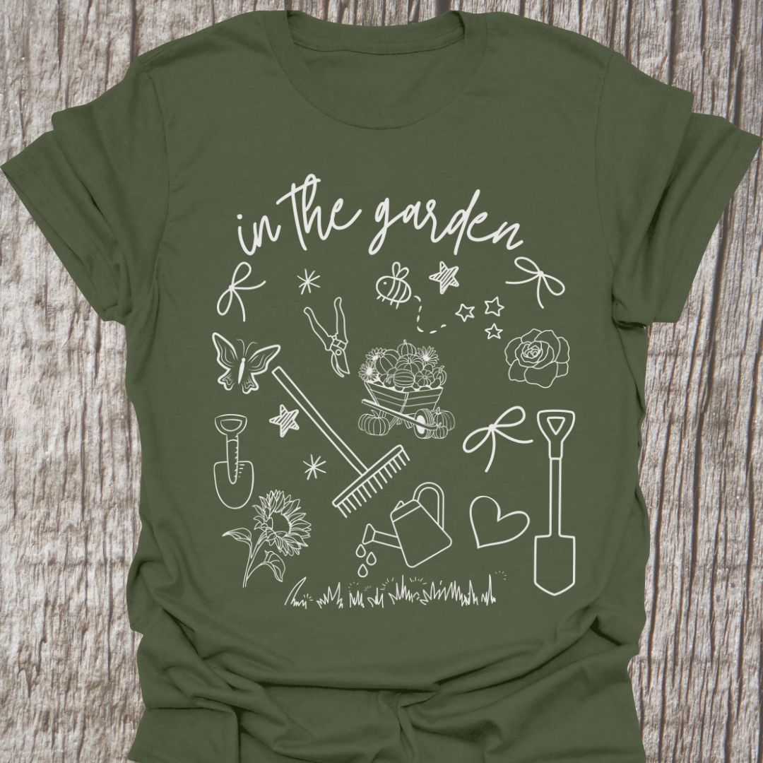 Garden Doodle on a T-shirt! This doodle has garden tools, flowers, grass, bees, butterfly and lots more, white images and text saying 'in the garden' on a military green t-shirt