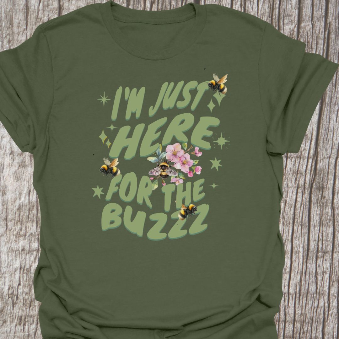 I am Just Here For The Buzz military green T-shirt, featuring a green text design adorned with bees and flowers for decoration