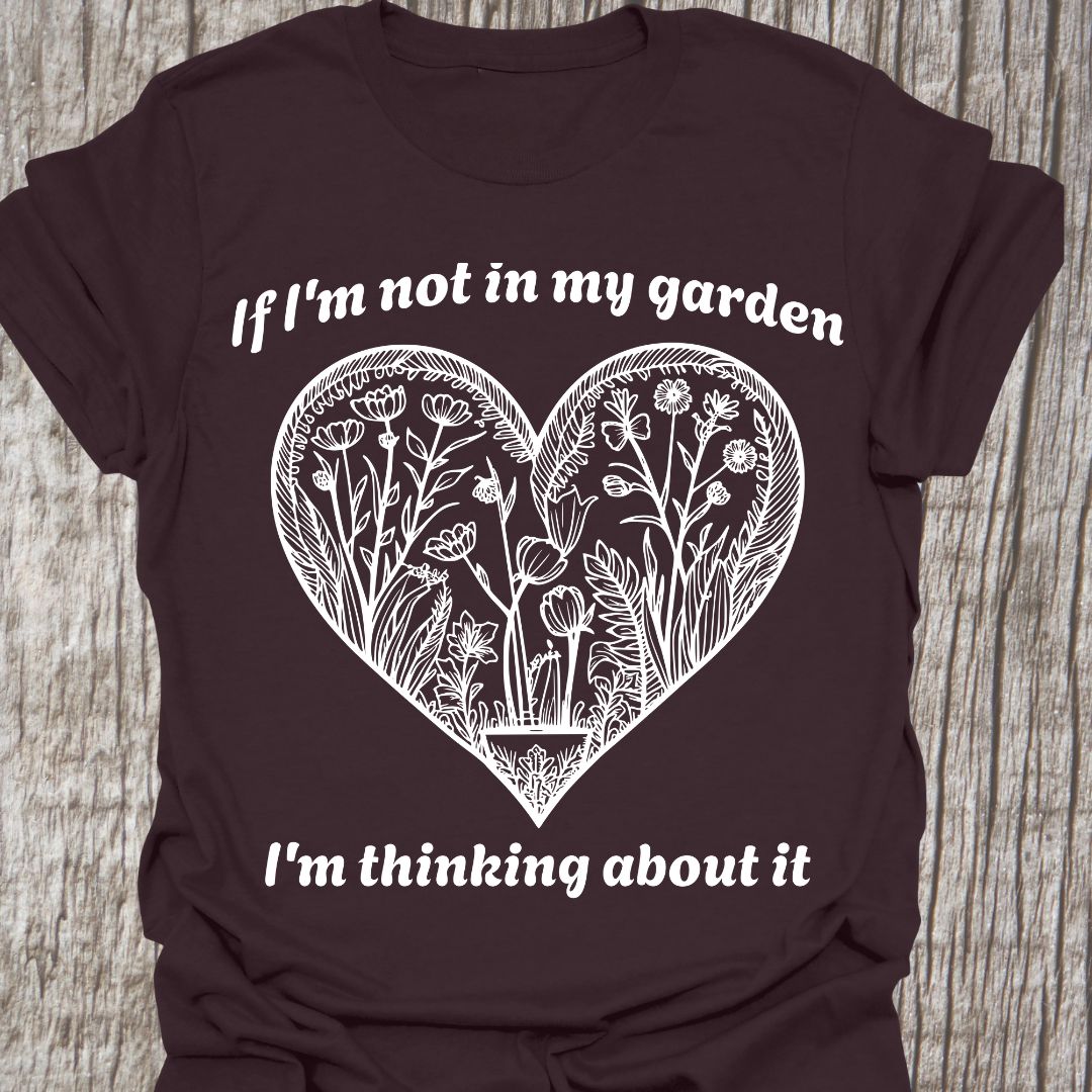 Text in white around a heart shape which contains flower images in white. Phrase above the heart is 'if I'm not in my garden' and below the heart 'I'm thinking about it', on a black t-shirt