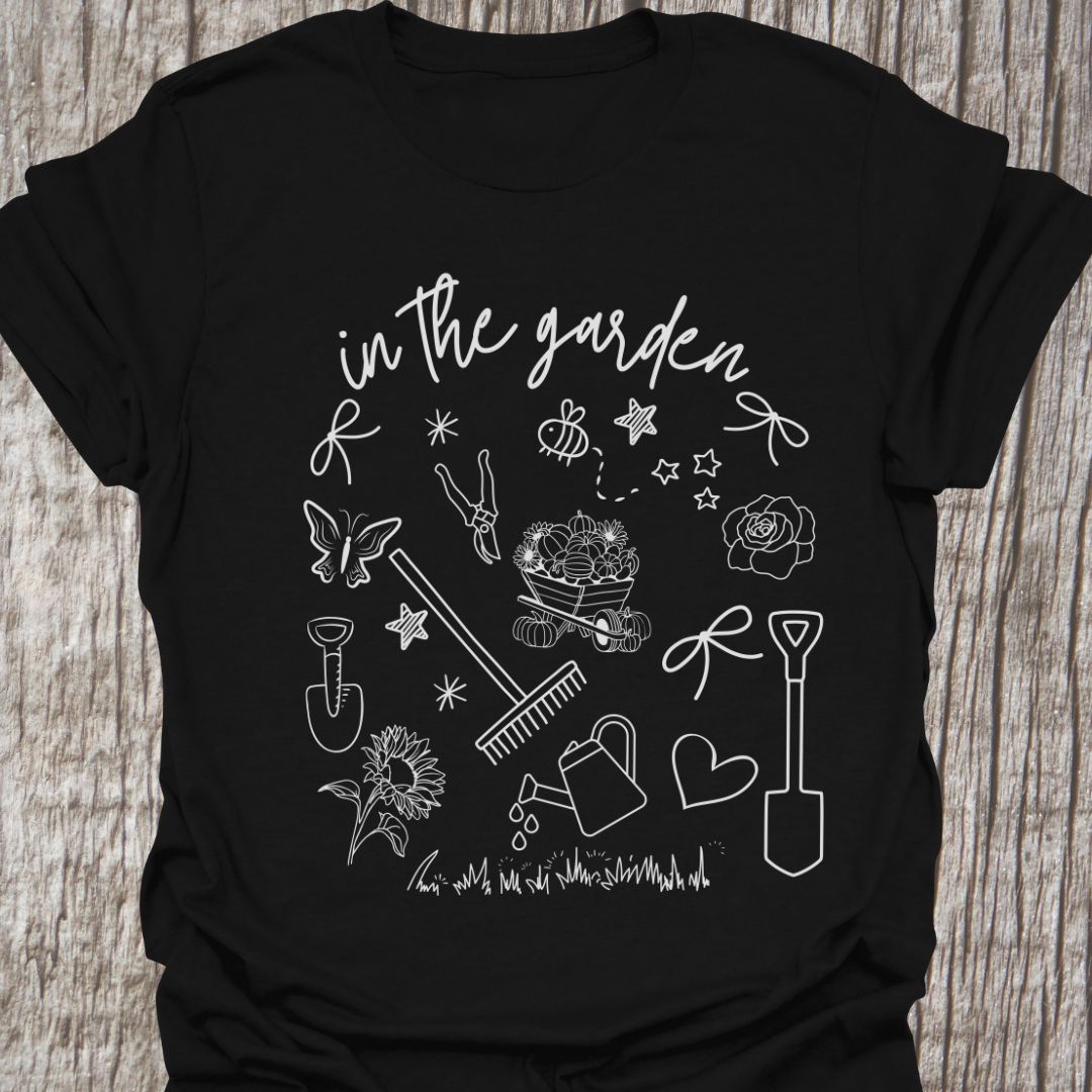 Garden Doodle on a T-shirt! This doodle has garden tools, flowers, grass, bees, butterfly and lots more, white images and text saying 'in the garden' on a black t-shirt