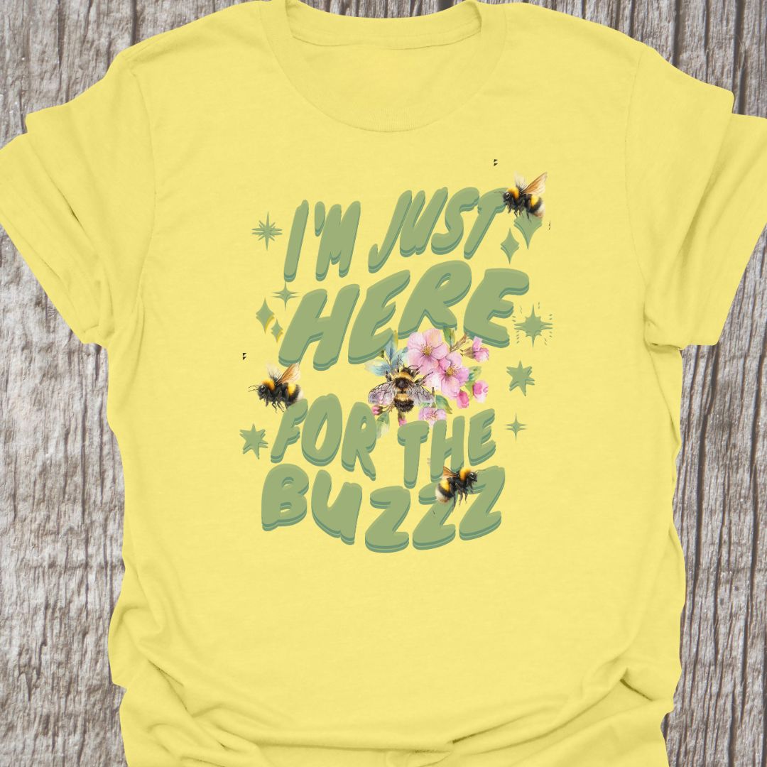 I am Just Here For The Buzz cornsilk T-shirt, featuring a green text design adorned with bees and flowers for decoration