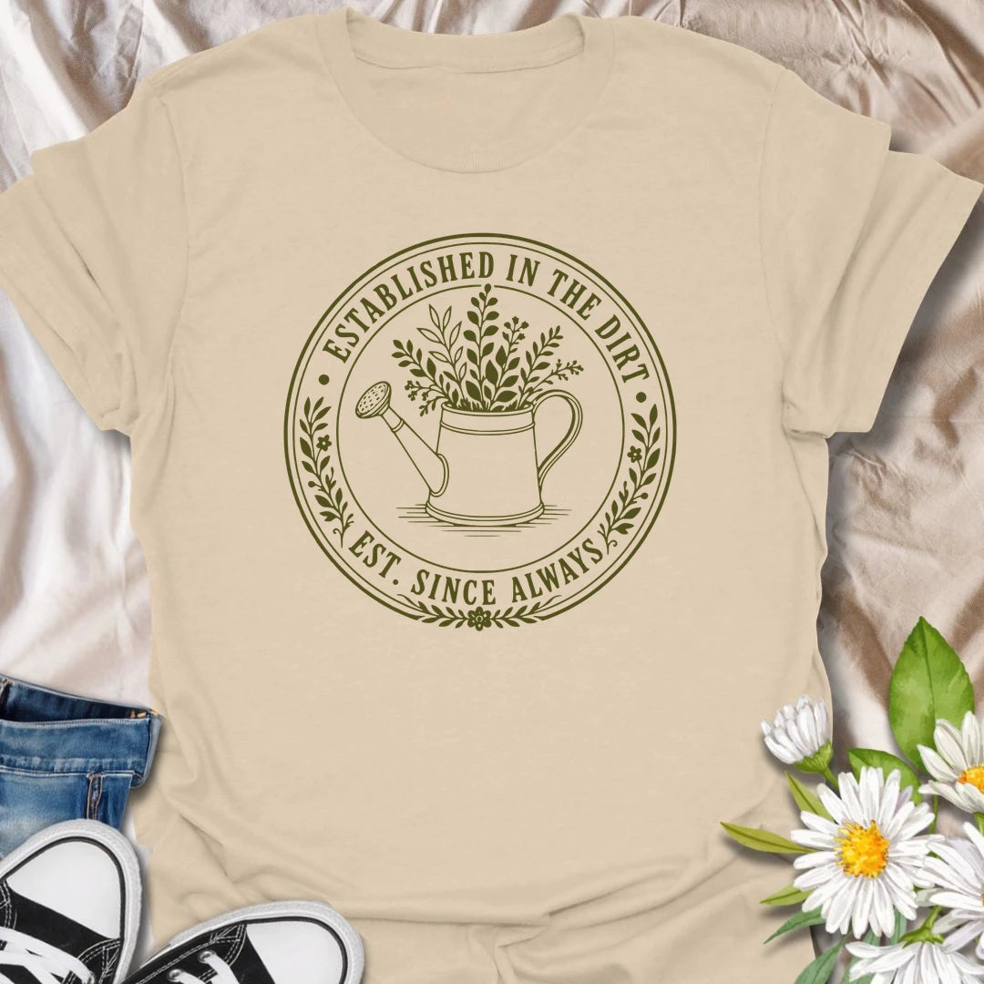 This Established In The Dirt t-shirt is made for gardeners who have always felt happiest with soil on their hands and something green to grow. Featuring a vintage-style circular badge with a watering can, leafy plant details, and the phrase Est. Since Always, this design has a simple botanical look that feels classic, earthy, and easy to wear. Perfect for gardeners, plant lovers, backyard growers, flower fans, vegetable gardeners, and anyone whose happy place is firmly rooted in the dirt.