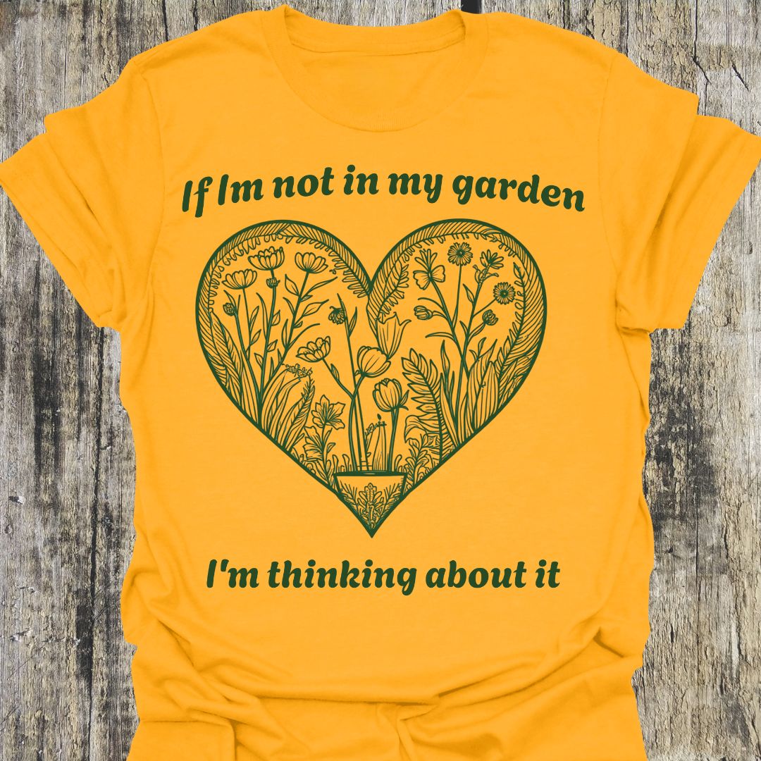 Text in green around a heart shape which contains flower images in green. Phrase above the heart is 'if I'm not in my garden' and below the heart 'I'm thinking about it', on a gold t-shirt