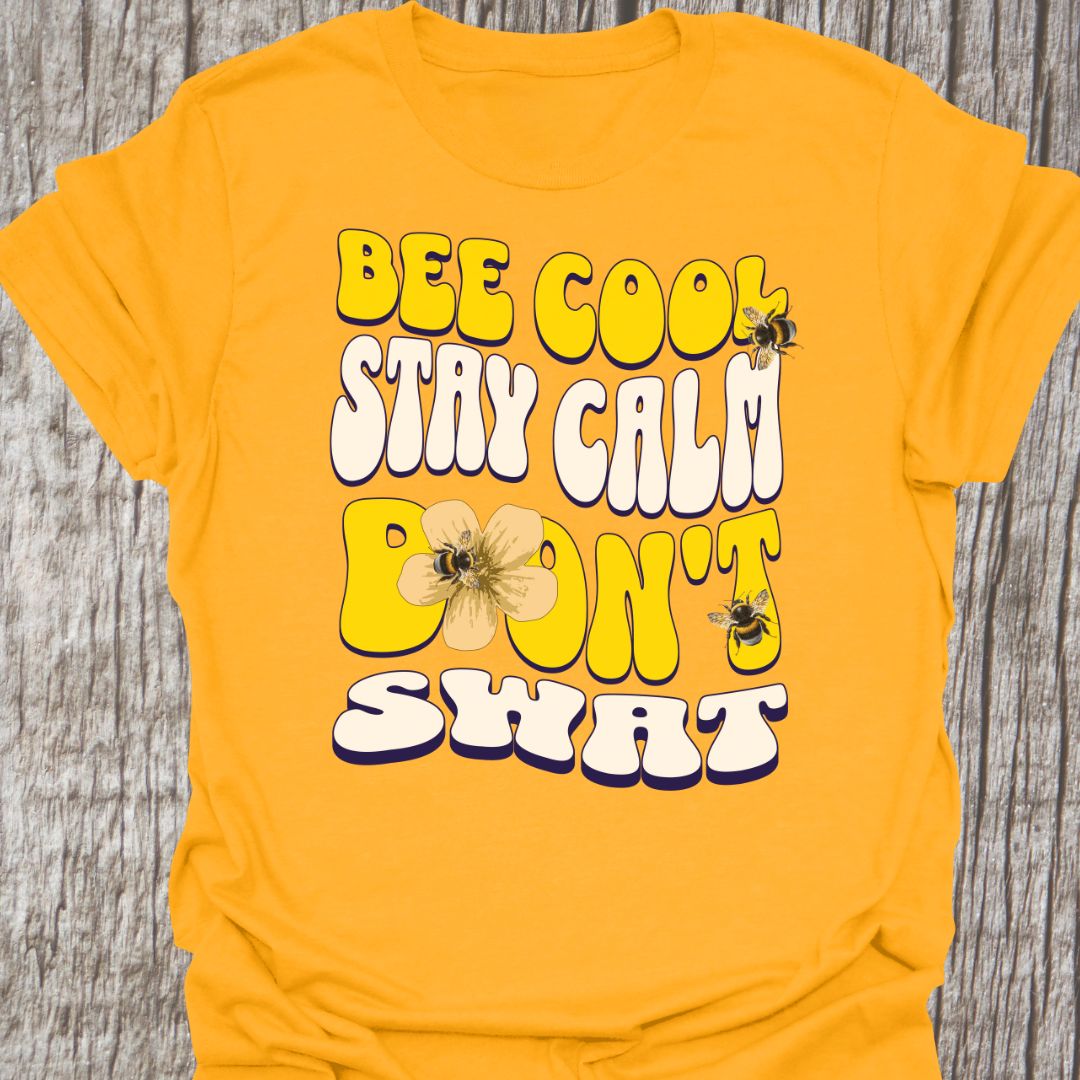 "Bee Cool, Stay Calm, Don't Swat" shaped text in white and yellow with images of bees and flowers. Gold colored T-shirt