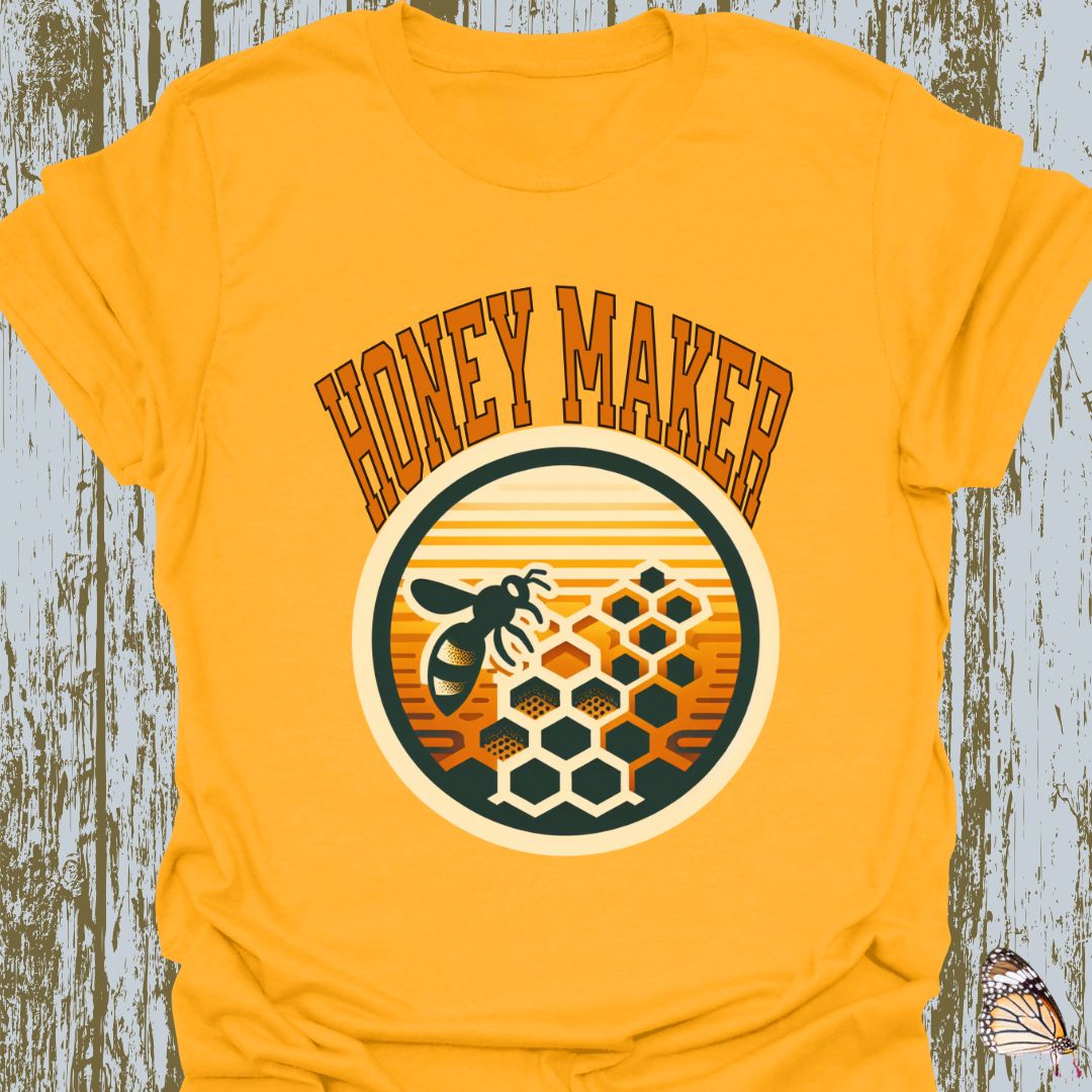 Gold T-shirt featuring a circular design with a bee and honeycomb, accompanied by the text "Honey Maker" in orange.