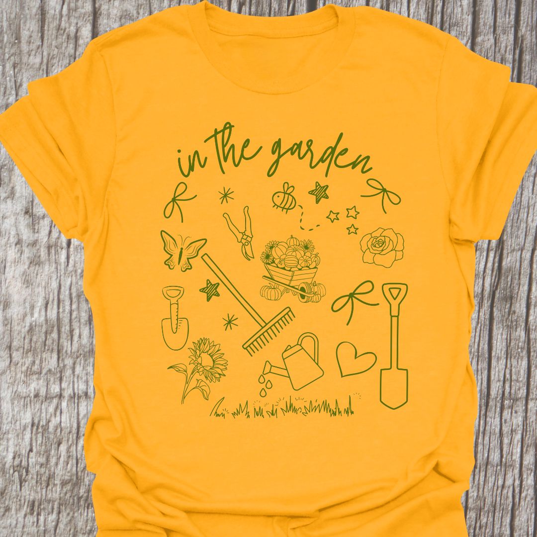 Garden Doodle on a T-shirt! This doodle has garden tools, flowers, grass, bees, butterfly and lots more, green images and text saying 'in the garden' on a gold t-shirt