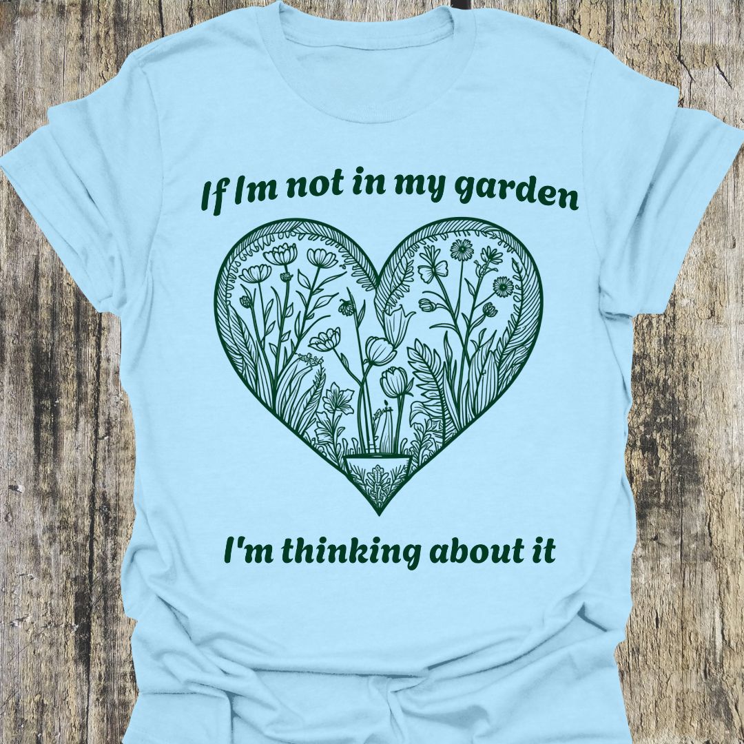 Text in green around a heart shape which contains flower images in green. Phrase above the heart is 'if I'm not in my garden' and below the heart 'I'm thinking about it', on a light blue t-shirt