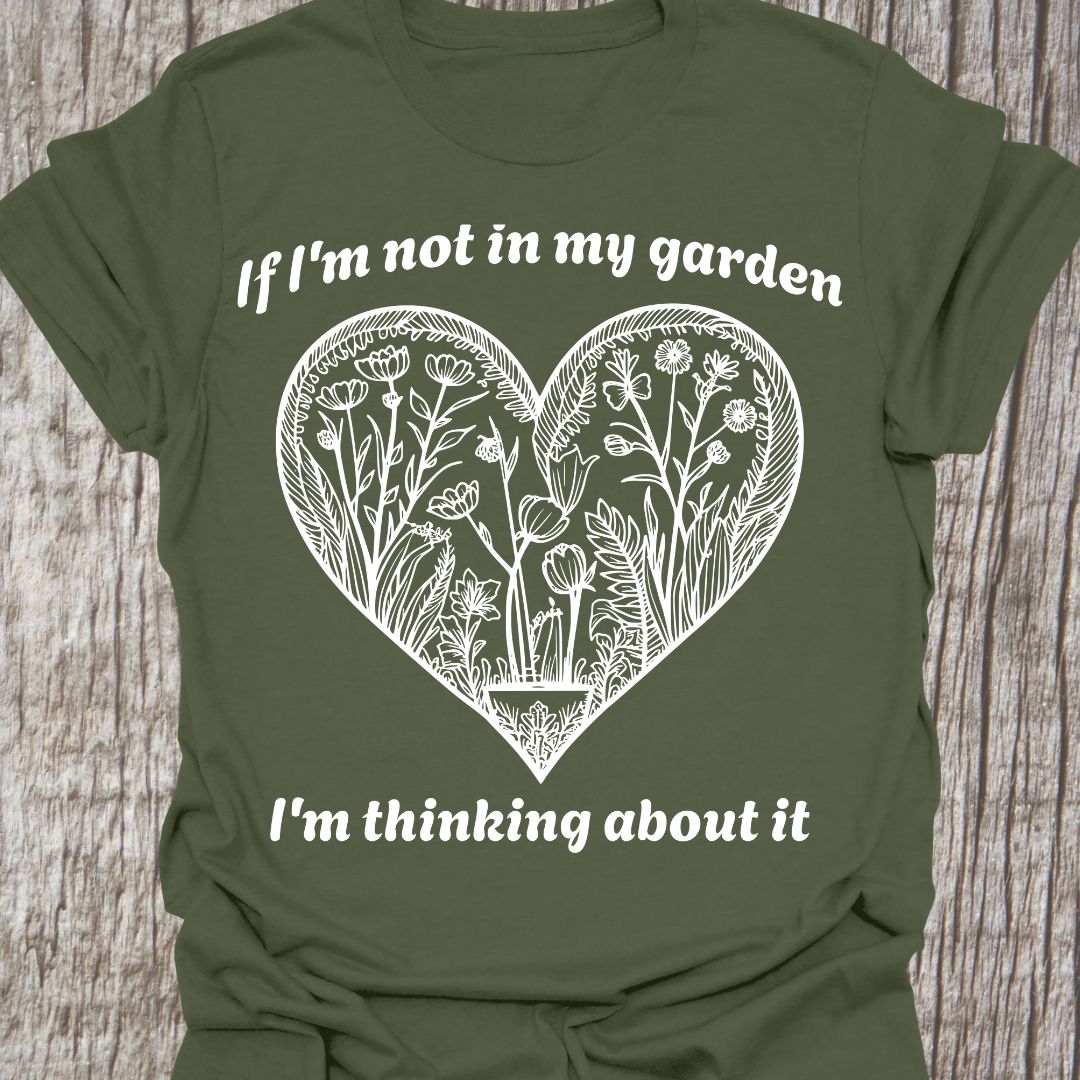 Text in white around a heart shape which contains flower images in white. Phrase above the heart is 'if I'm not in my garden' and below the heart 'I'm thinking about it', on a military green t-shirt