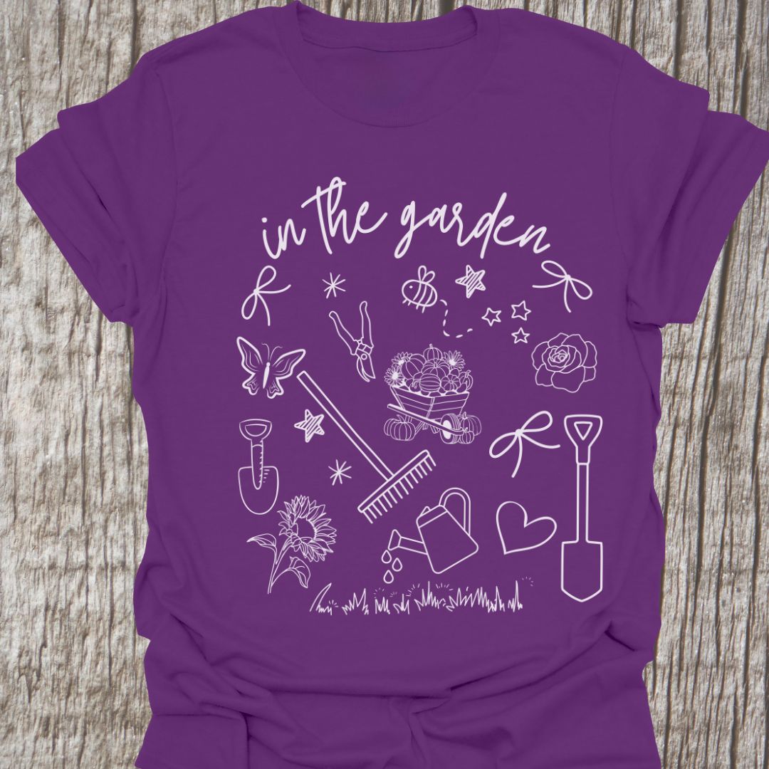 Garden Doodle on a T-shirt! This doodle has garden tools, flowers, grass, bees, butterfly and lots more, white images and text saying 'in the garden' on a purple t-shirt