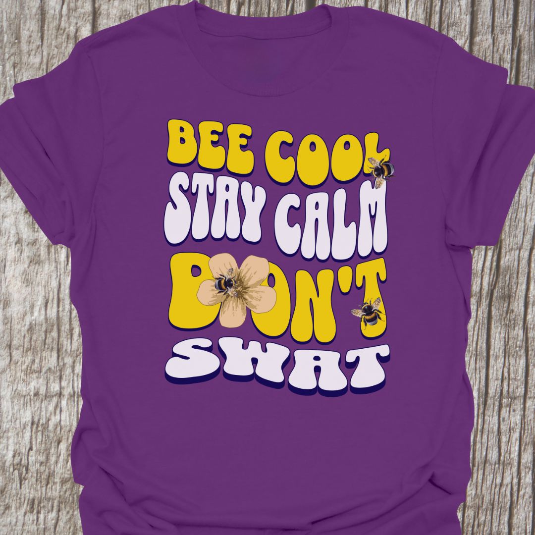 "Bee Cool, Stay Calm, Don't Swat" shaped text in white and yellow with images of bees and flowers. Purple colored T-shirt