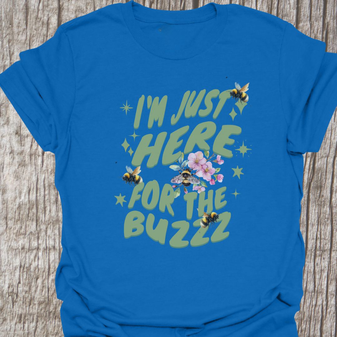I am Just Here For The Buzz royal blue T-shirt, featuring a green text design adorned with bees and flowers for decoration