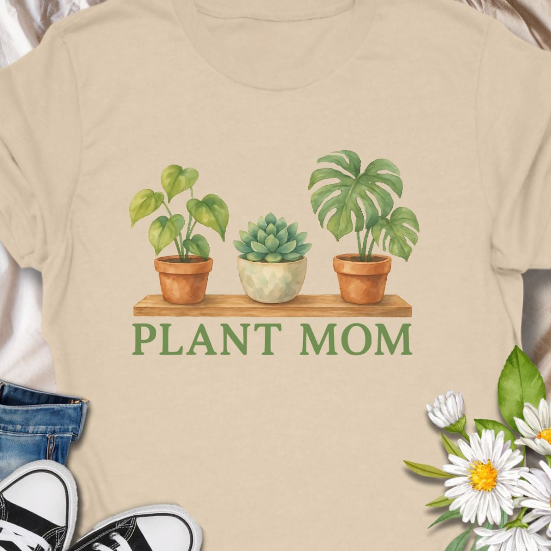 Show off your green thumb with this charming “Plant Mom” t-shirt featuring potted plants on a wooden shelf. Ideal for plant lovers, indoor gardeners, or anyone who adores succulents and tropical houseplants. This tee makes a perfect gift for Mother's Day, birthdays, or just to treat yourself with botanical flair.