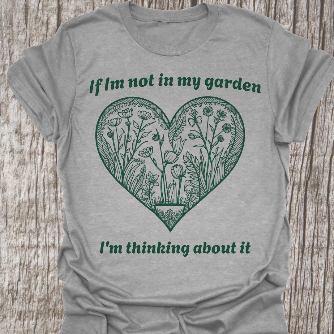 Text in green around a heart shape which contains flower images in green. Phrase above the heart is 'if I'm not in my garden' and below the heart 'I'm thinking about it', on a sport grey t-shirt