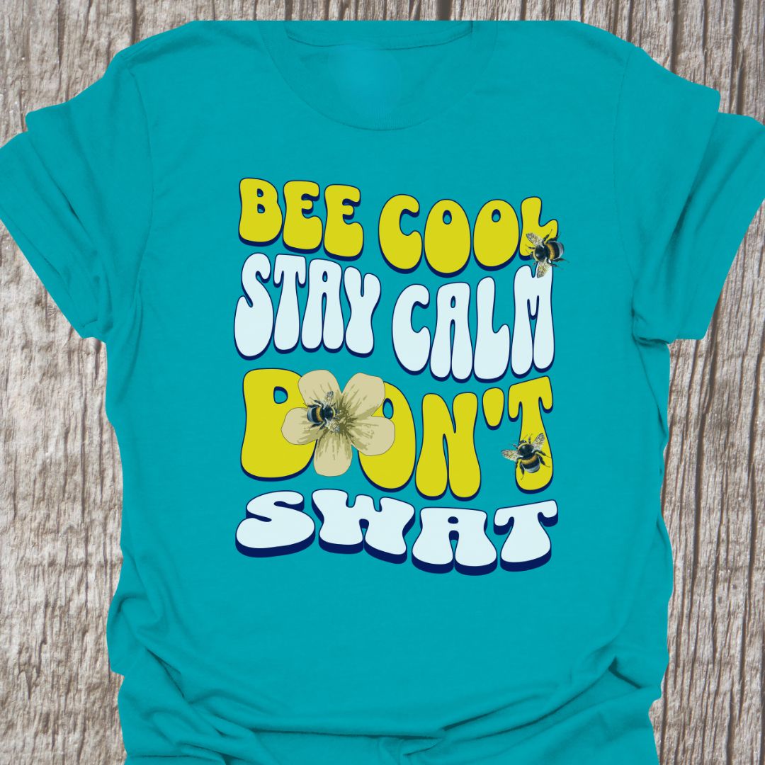 "Bee Cool, Stay Calm, Don't Swat" shaped text in white and yellow with images of bees and flowers. Tropical blue colored T-shirt