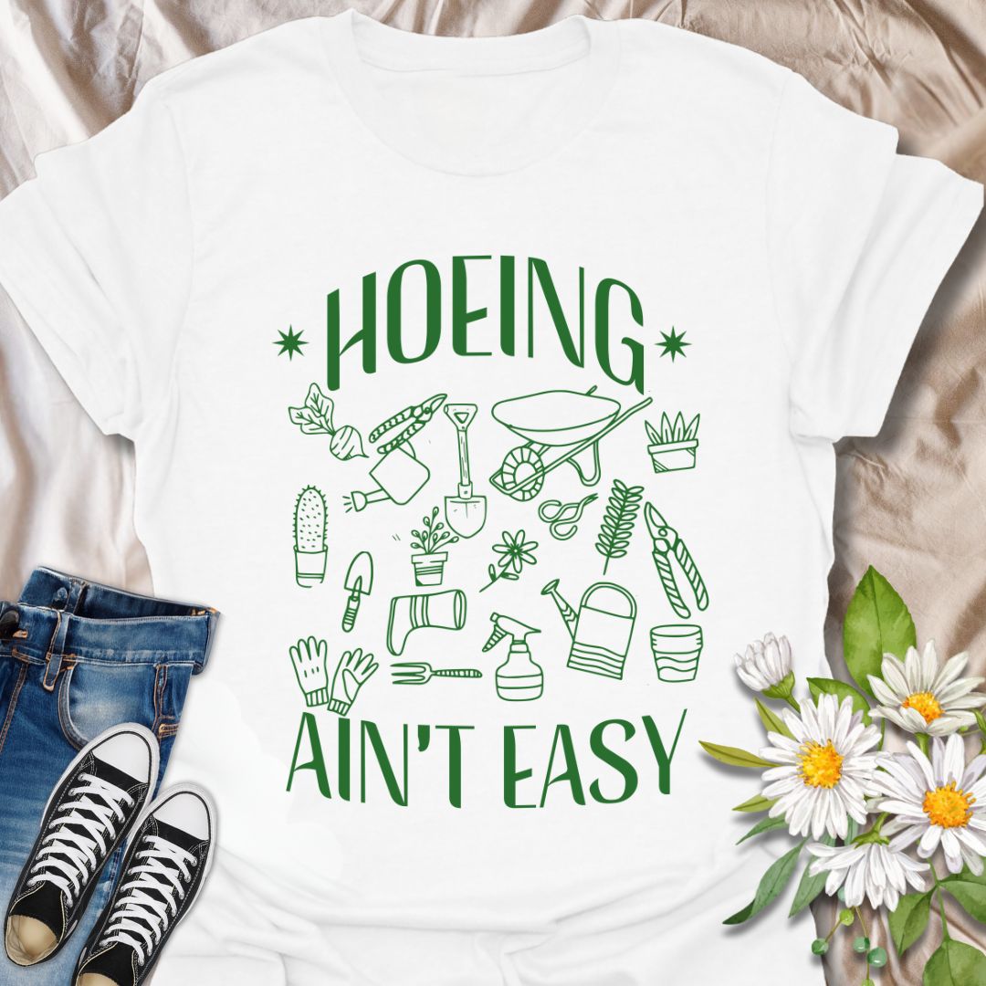 Funny gardening t-shirt with cute garden tools and “Hoeing Ain’t Easy” slogan. Perfect gift for plant lovers, gardeners, or anyone with a green thumb and a sense of humor. White