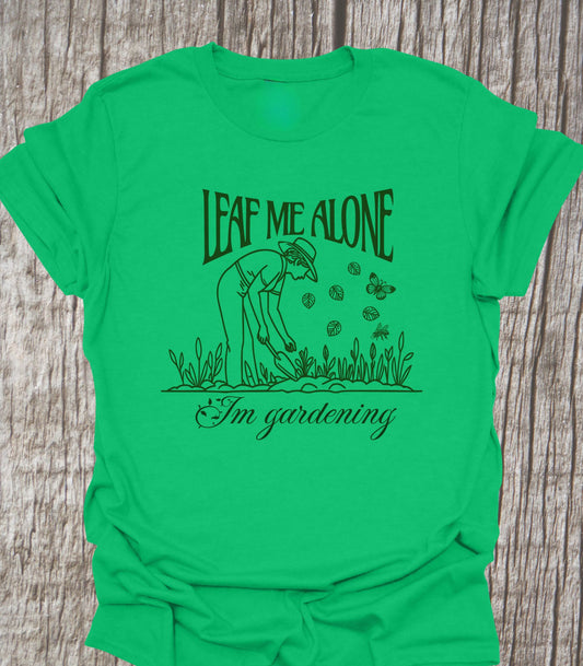 T-shirt in Irish Green with the text 'Leaf me alone' above an image of a man gardening and 'I'm gardening' below the image. Text and design all in one color.