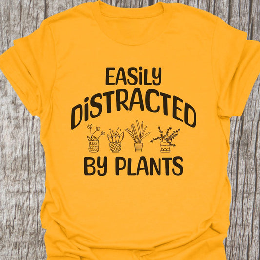 Easily Distracted By Plants in black Text with image of four small pot plants, all in black. This is on a gold colored T-shirt