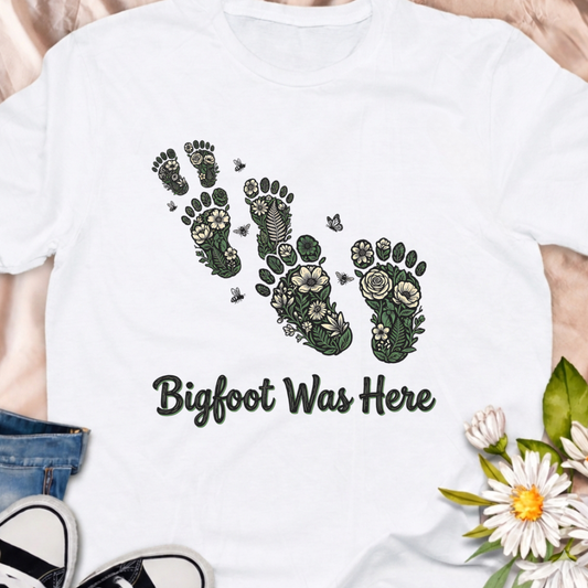 Whimsical “Bigfoot Was Here” t-shirt featuring floral footprint artwork with leaves, wildflowers and butterflies. Perfect for plant lovers, hikers, gardeners and cottagecore fans who love a touch of woodland mystery.