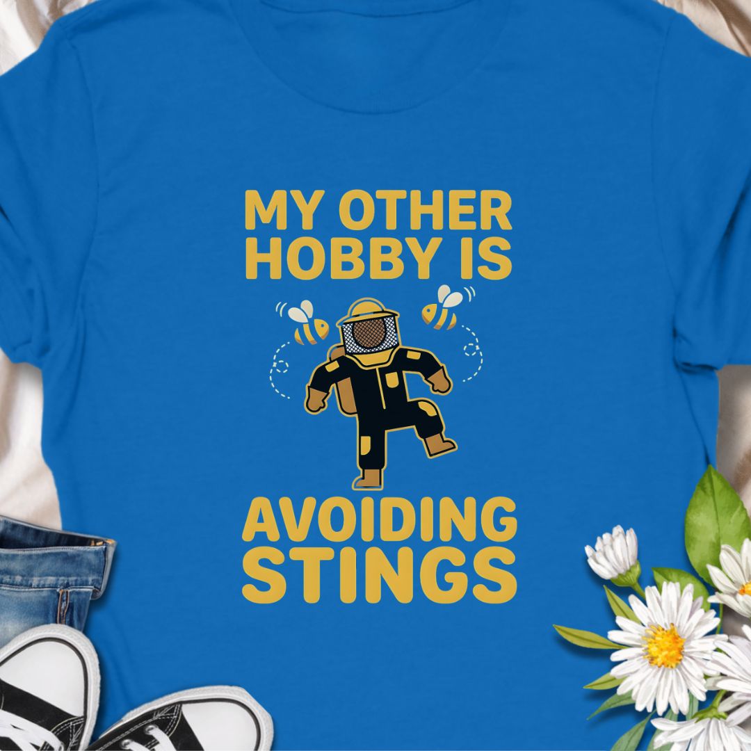 My other hobby is avoiding stings. A funny beekeeper shirt featuring a playful bee graphic, perfect for beekeepers, honey lovers, and anyone obsessed with bees. This soft unisex tee makes a great gift for apiarists, gardeners, and pollinator supporters.