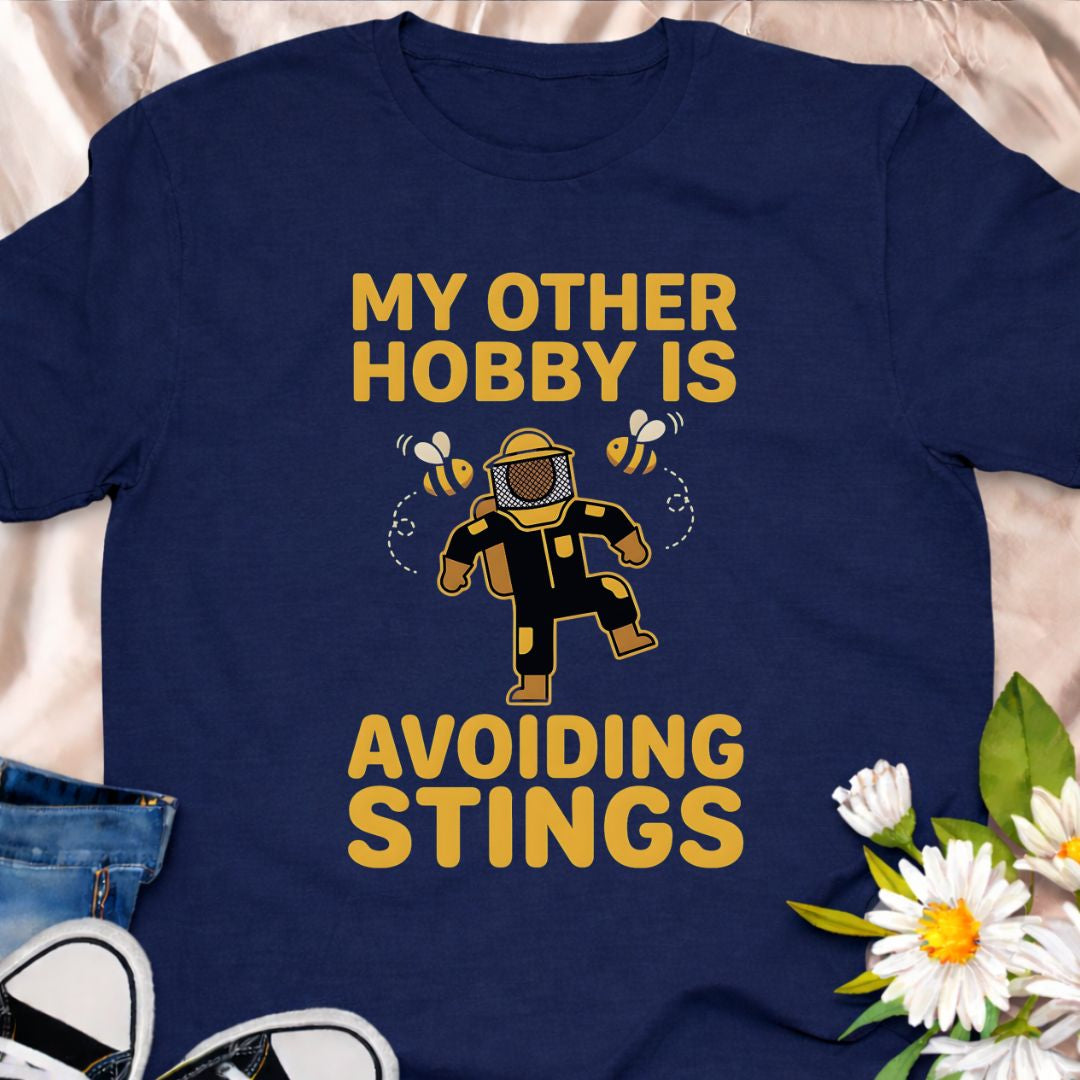 My other hobby is avoiding stings. A funny beekeeper shirt featuring a playful bee graphic, perfect for beekeepers, honey lovers, and anyone obsessed with bees. This soft unisex tee makes a great gift for apiarists, gardeners, and pollinator supporters.