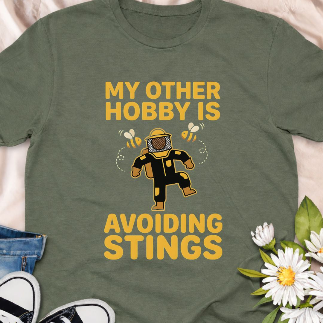 My other hobby is avoiding stings. A funny beekeeper shirt featuring a playful bee graphic, perfect for beekeepers, honey lovers, and anyone obsessed with bees. This soft unisex tee makes a great gift for apiarists, gardeners, and pollinator supporters.
