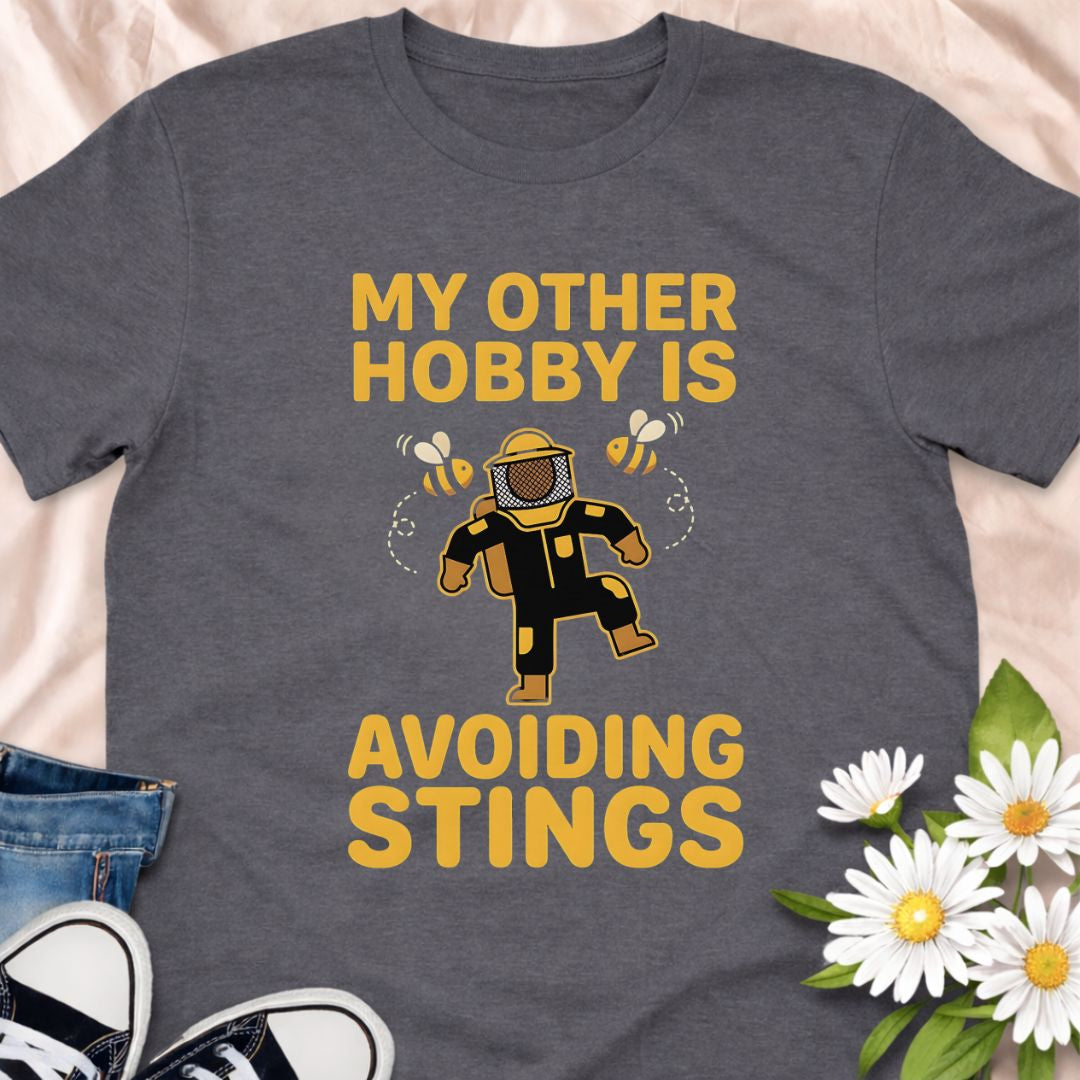 My other hobby is avoiding stings. A funny beekeeper shirt featuring a playful bee graphic, perfect for beekeepers, honey lovers, and anyone obsessed with bees. This soft unisex tee makes a great gift for apiarists, gardeners, and pollinator supporters.