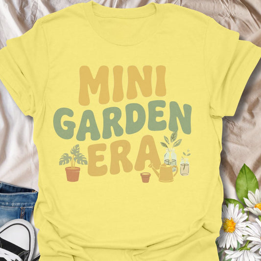 Retro-inspired plant lover t-shirt featuring the phrase “Mini Garden Era” with charming plant and watering can graphics. A fun tee for plant parents, indoor gardeners, houseplant lovers, and anyone embracing their small-space gardening phase.