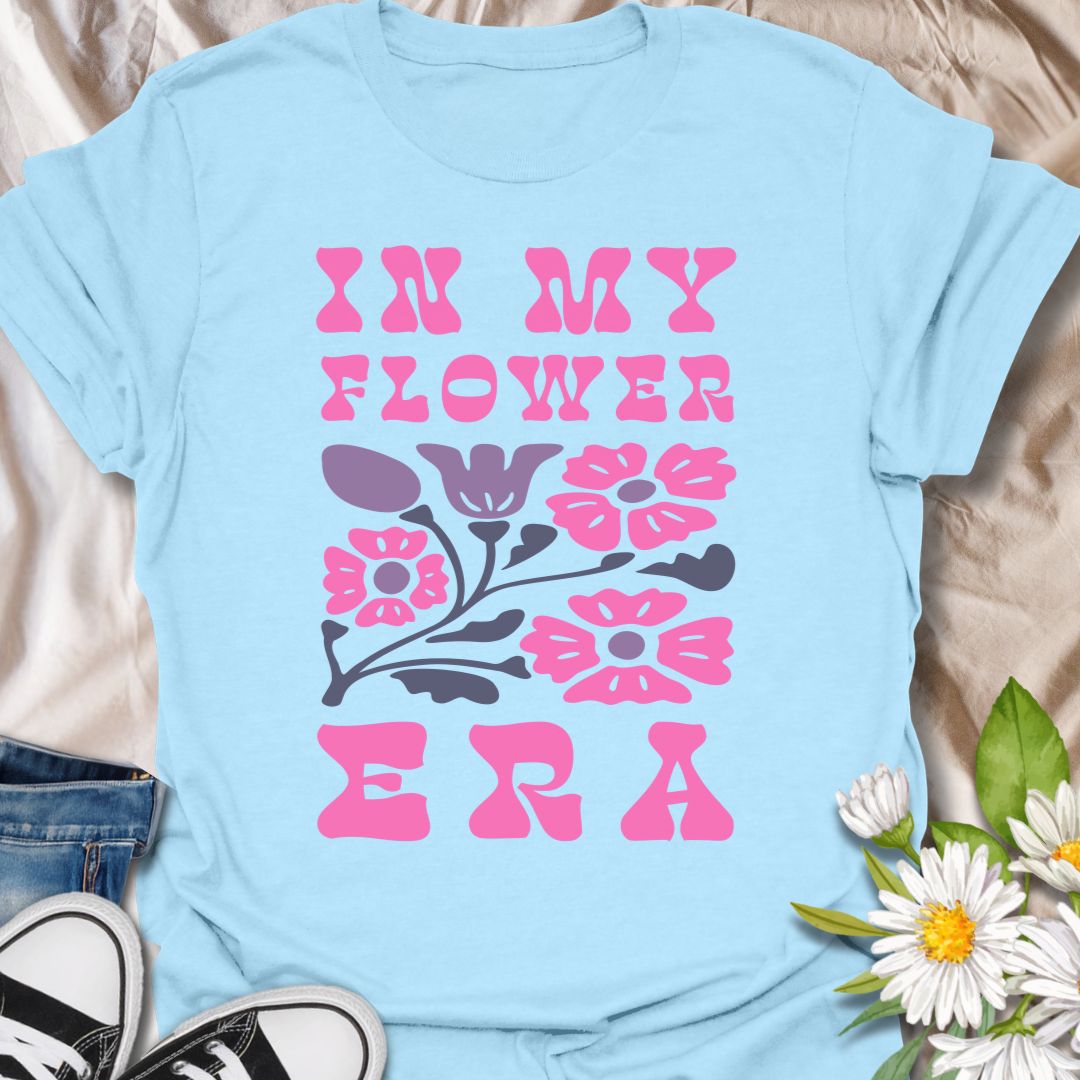This In My Flower Era t-shirt is made for flower lovers who are fully embracing their blooming, botanical, garden-girl phase. Featuring bold retro pink lettering with a simple floral graphic in soft purple and navy tones, this design has a playful vintage-inspired look that feels cute, bright, and easy to wear. Perfect for gardeners, flower fans, plant lovers, cottagecore style lovers, botanical art fans, and anyone who is proudly in their flower era.