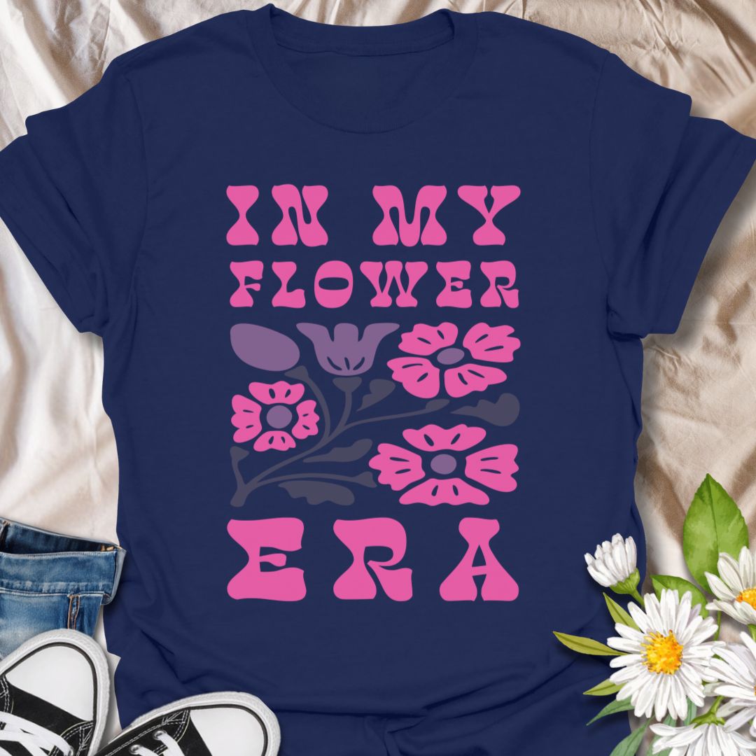 This In My Flower Era t-shirt is made for flower lovers who are fully embracing their blooming, botanical, garden-girl phase. Featuring bold retro pink lettering with a simple floral graphic in soft purple and navy tones, this design has a playful vintage-inspired look that feels cute, bright, and easy to wear. Perfect for gardeners, flower fans, plant lovers, cottagecore style lovers, botanical art fans, and anyone who is proudly in their flower era.