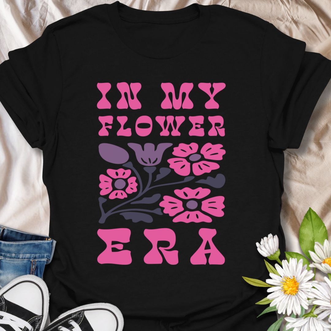 This In My Flower Era t-shirt is made for flower lovers who are fully embracing their blooming, botanical, garden-girl phase. Featuring bold retro pink lettering with a simple floral graphic in soft purple and navy tones, this design has a playful vintage-inspired look that feels cute, bright, and easy to wear. Perfect for gardeners, flower fans, plant lovers, cottagecore style lovers, botanical art fans, and anyone who is proudly in their flower era.