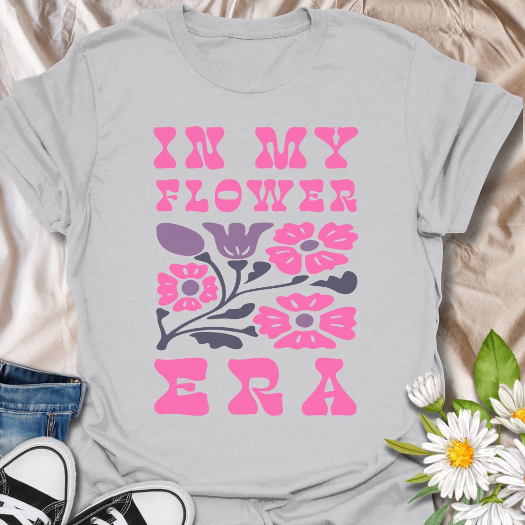 This In My Flower Era t-shirt is made for flower lovers who are fully embracing their blooming, botanical, garden-girl phase. Featuring bold retro pink lettering with a simple floral graphic in soft purple and navy tones, this design has a playful vintage-inspired look that feels cute, bright, and easy to wear. Perfect for gardeners, flower fans, plant lovers, cottagecore style lovers, botanical art fans, and anyone who is proudly in their flower era.