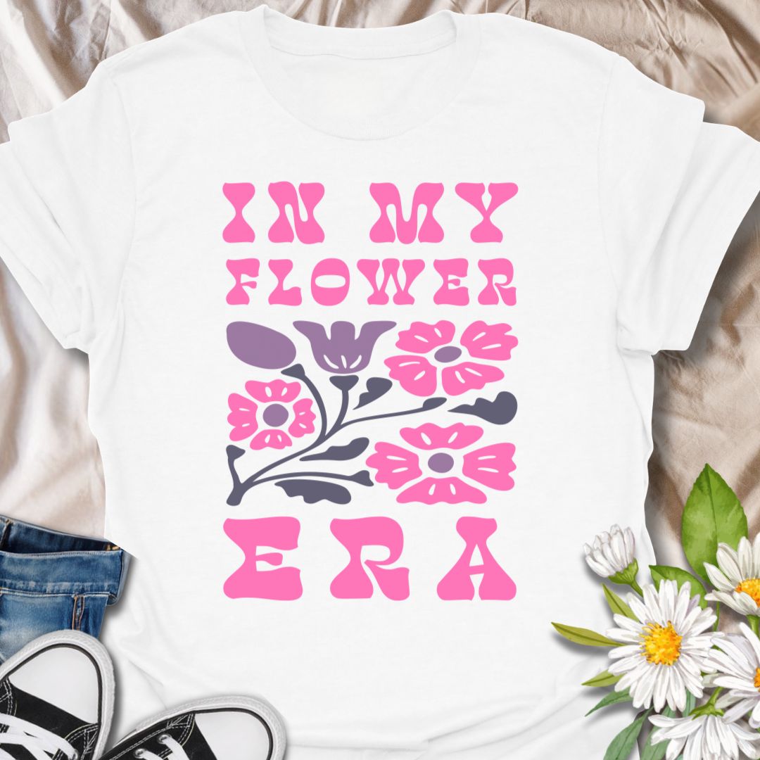 This In My Flower Era t-shirt is made for flower lovers who are fully embracing their blooming, botanical, garden-girl phase. Featuring bold retro pink lettering with a simple floral graphic in soft purple and navy tones, this design has a playful vintage-inspired look that feels cute, bright, and easy to wear. Perfect for gardeners, flower fans, plant lovers, cottagecore style lovers, botanical art fans, and anyone who is proudly in their flower era.