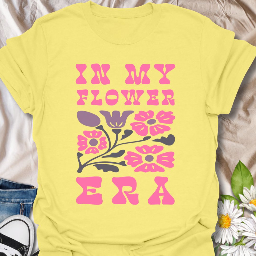 This In My Flower Era t-shirt is made for flower lovers who are fully embracing their blooming, botanical, garden-girl phase. Featuring bold retro pink lettering with a simple floral graphic in soft purple and navy tones, this design has a playful vintage-inspired look that feels cute, bright, and easy to wear. Perfect for gardeners, flower fans, plant lovers, cottagecore style lovers, botanical art fans, and anyone who is proudly in their flower era.