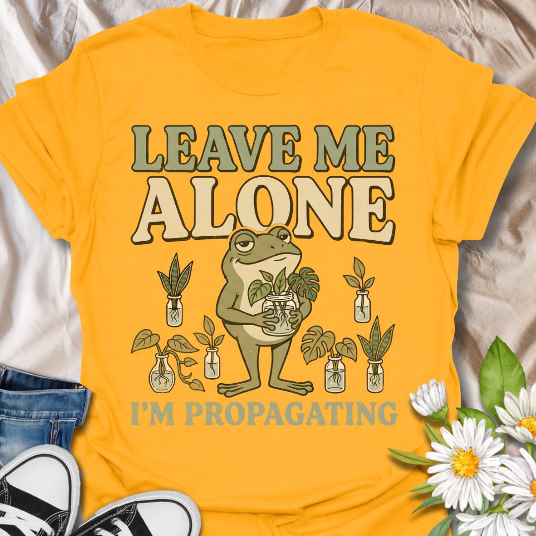 This Leave Me Alone I’m Propagating t-shirt is made for plant lovers who take cuttings, jars, roots, and quiet plant time very seriously. Featuring a smug cartoon frog holding propagated plant cuttings, surrounded by propagation jars, leafy plants, and bold retro lettering, this design has a funny botanical vibe with plenty of plant-parent attitude. Perfect for houseplant lovers, plant moms, propagation fans, indoor gardeners, frog lovers, and anyone who would rather be rooting cuttings than talking to peop