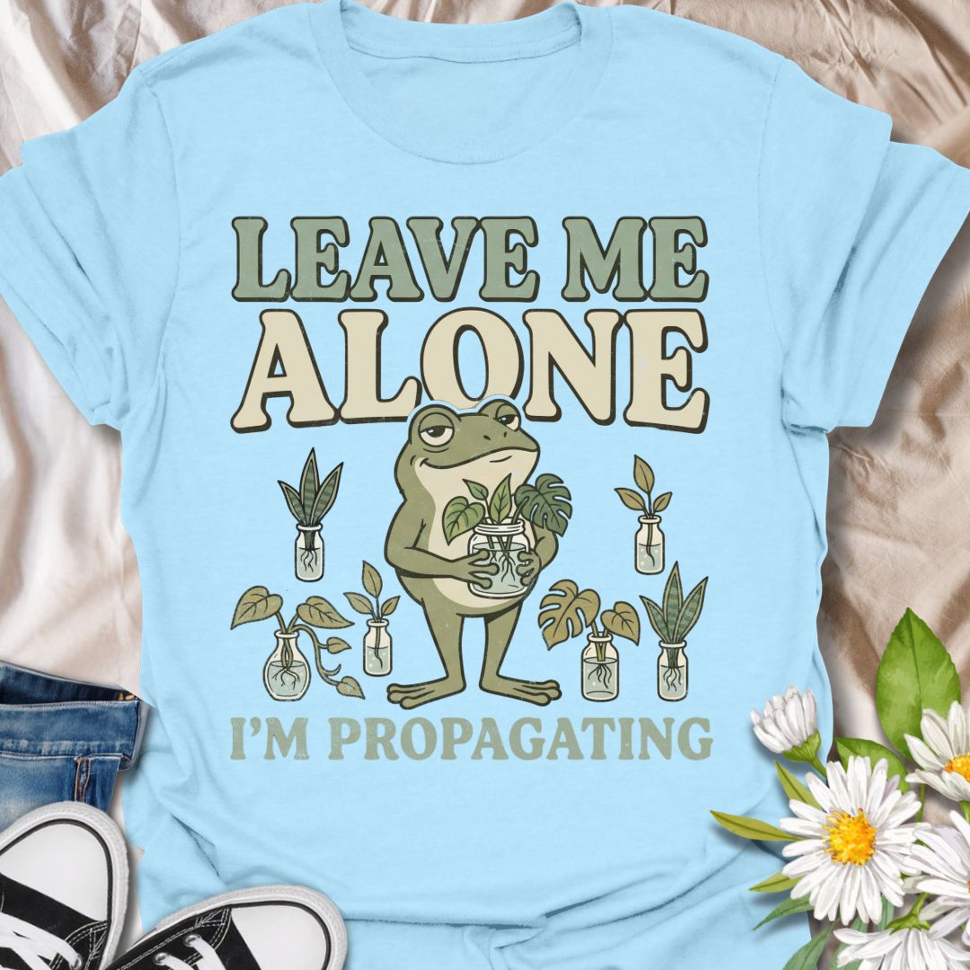 This Leave Me Alone I’m Propagating t-shirt is made for plant lovers who take cuttings, jars, roots, and quiet plant time very seriously. Featuring a smug cartoon frog holding propagated plant cuttings, surrounded by propagation jars, leafy plants, and bold retro lettering, this design has a funny botanical vibe with plenty of plant-parent attitude. Perfect for houseplant lovers, plant moms, propagation fans, indoor gardeners, frog lovers, and anyone who would rather be rooting cuttings than talking to peop