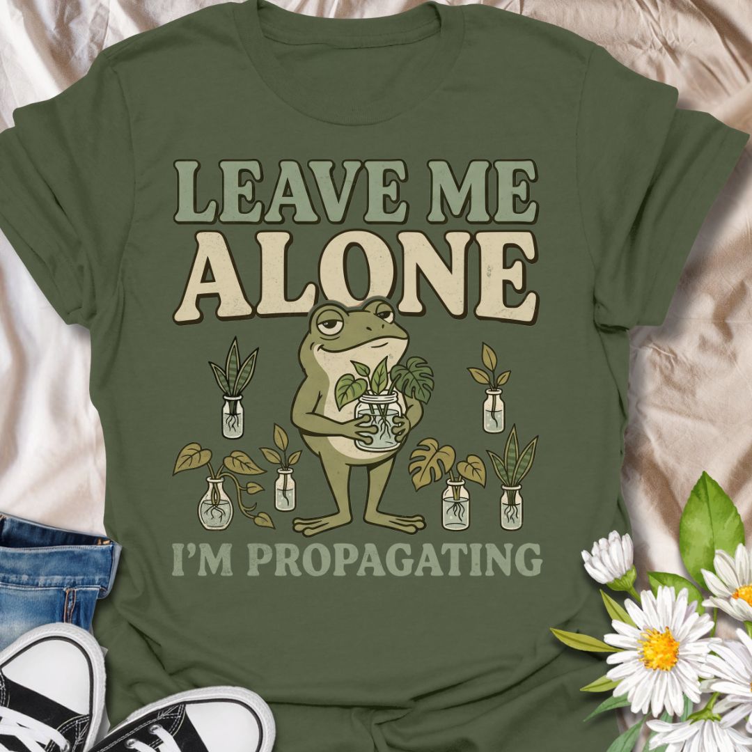 This Leave Me Alone I’m Propagating t-shirt is made for plant lovers who take cuttings, jars, roots, and quiet plant time very seriously. Featuring a smug cartoon frog holding propagated plant cuttings, surrounded by propagation jars, leafy plants, and bold retro lettering, this design has a funny botanical vibe with plenty of plant-parent attitude. Perfect for houseplant lovers, plant moms, propagation fans, indoor gardeners, frog lovers, and anyone who would rather be rooting cuttings than talking to peop