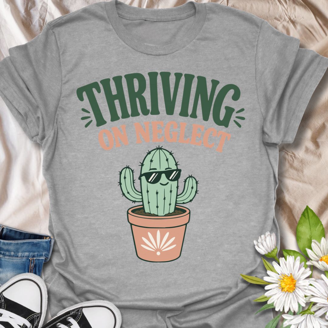 This Thriving On Neglect t-shirt is made for plant lovers who relate a little too much to low-maintenance cactus energy. Featuring a cool potted cactus wearing sunglasses with bold retro lettering in green, peach, and soft cream, this design has a funny, easygoing botanical vibe. Perfect for cactus lovers, succulent fans, plant moms, plant dads, houseplant collectors, and anyone who is doing surprisingly well with minimal care.