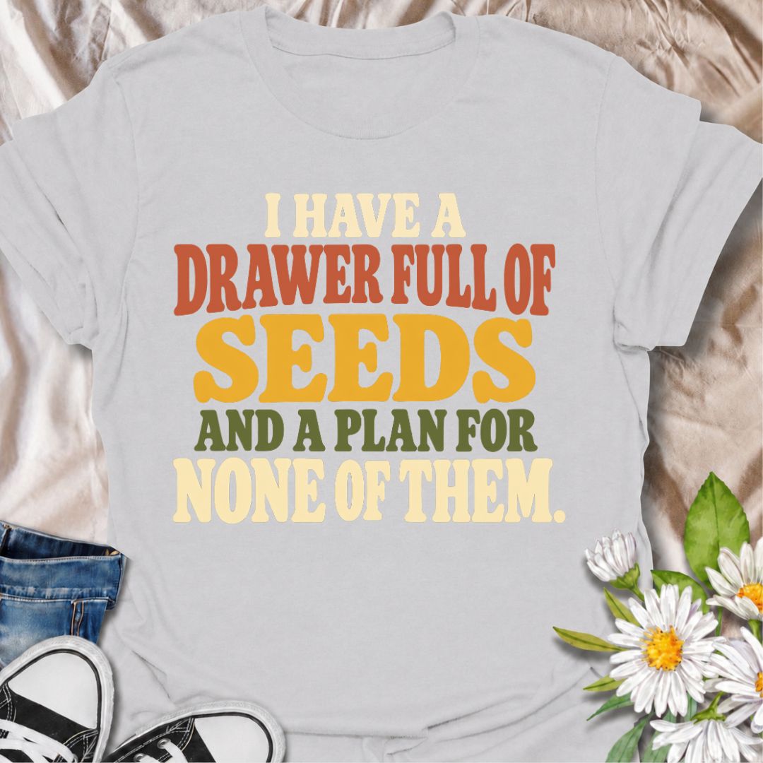 A funny gardening T-shirt for anyone who has collected far more seeds than they have actual planting plans. The phrase “I Have a Drawer Full of Seeds and a Plan for None of Them” captures the wonderfully chaotic side of gardening with dry, relatable humor. Its bold retro typography makes the joke easy to read while keeping the design clean and wearable. It makes a great gift for seed savers, vegetable gardeners, flower growers, and anyone who cannot resist another packet at the garden center. Ideal for gard