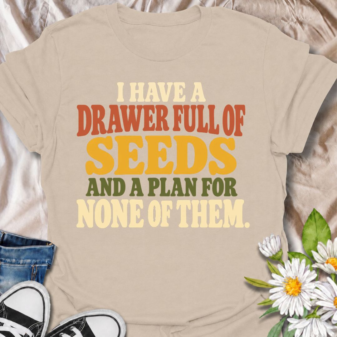 A funny gardening T-shirt for anyone who has collected far more seeds than they have actual planting plans. The phrase “I Have a Drawer Full of Seeds and a Plan for None of Them” captures the wonderfully chaotic side of gardening with dry, relatable humor. Its bold retro typography makes the joke easy to read while keeping the design clean and wearable. It makes a great gift for seed savers, vegetable gardeners, flower growers, and anyone who cannot resist another packet at the garden center. Ideal for gard