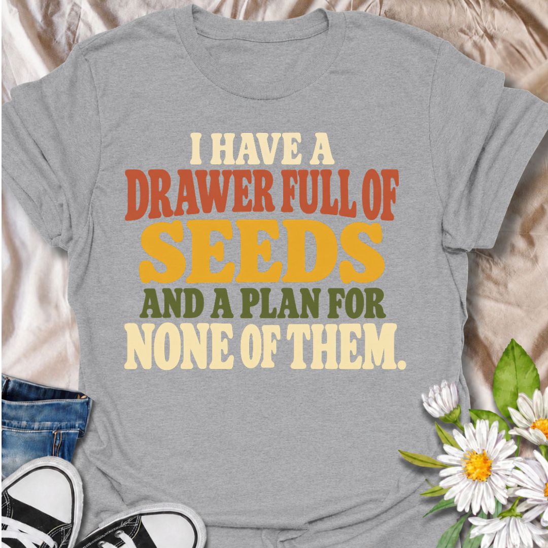 A funny gardening T-shirt for anyone who has collected far more seeds than they have actual planting plans. The phrase “I Have a Drawer Full of Seeds and a Plan for None of Them” captures the wonderfully chaotic side of gardening with dry, relatable humor. Its bold retro typography makes the joke easy to read while keeping the design clean and wearable. It makes a great gift for seed savers, vegetable gardeners, flower growers, and anyone who cannot resist another packet at the garden center. Ideal for gard