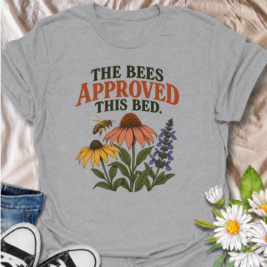 A cheerful gardening T-shirt for anyone who takes pride in growing flowers the pollinators love. The phrase “The Bees Approved This Bed” pairs perfectly with coneflowers, black-eyed Susans, salvia, and a visiting bee for a garden design with real pollinator appeal. It is ideal for flower gardeners, wildlife gardeners, native plant lovers, and anyone creating a bee-friendly backyard. The design makes a lovely gift for gardeners who enjoy supporting bees while filling their beds with color. Perfect for garden