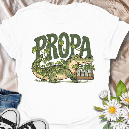 A funny plant propagation T-shirt built around the “propa-gator” pun, featuring an alligator surrounded by trailing plants and rooted cuttings. The playful design is perfect for houseplant lovers, propagation fans, plant parents, and anyone whose counters are filling up with jars of cuttings. It combines botanical humor with a bold character-led illustration that feels distinctive and easy to wear. This makes a great gift for pothos lovers, indoor gardeners, and anyone who is always rooting one more plant. 