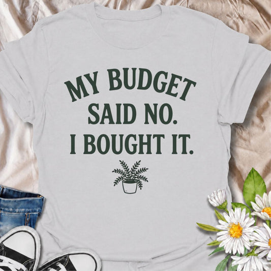 A funny plant T-shirt for anyone who knows a sensible budget can disappear the moment a new plant comes into view. The phrase “My Budget Said No. I Bought It.” captures the reality of impulsive plant shopping with simple, relatable humor. Featuring a small potted plant beneath bold retro typography, the design stays clean, readable, and easy to wear. It makes a great gift for plant parents, houseplant collectors, and nursery regulars who can never resist one more purchase. Perfect for plant swaps, garden ce