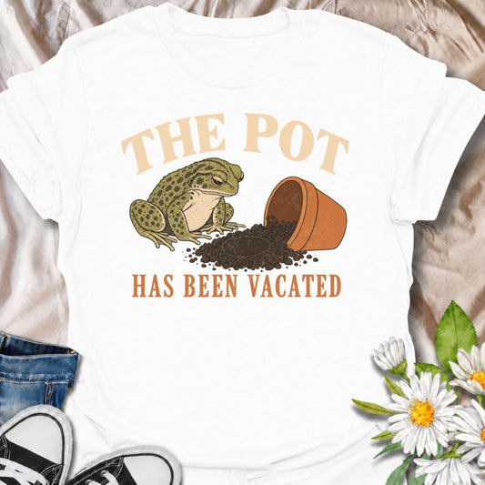A funny plant T-shirt for anyone who knows an empty pot never stays empty for long. Featuring a deadpan frog beside an overturned planter and a suspiciously vacant patch of soil, this design gives “The Pot Has Been Vacated” a dry, slightly absurd sense of humor. It is perfect for houseplant lovers, plant parents, gardeners, and anyone who treats an empty pot as an invitation to buy something new. The vintage-style illustration makes it feel distinctive while still being easy to wear. A fun gift for plant co
