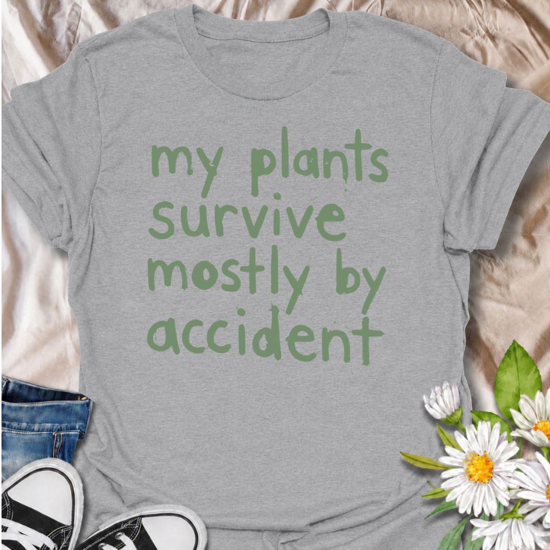 A funny plant T-shirt for anyone whose houseplants are doing surprisingly well despite a slightly questionable care routine. The phrase “My Plants Survive Mostly by Accident” delivers dry, self-deprecating humor that plant parents and indoor gardeners will instantly relate to. Its simple hand-drawn typography keeps the design casual, modern, and easy to wear. It makes a great gift for houseplant lovers, accidental green thumbs, and anyone who is still figuring out what their plants actually need. Perfect fo