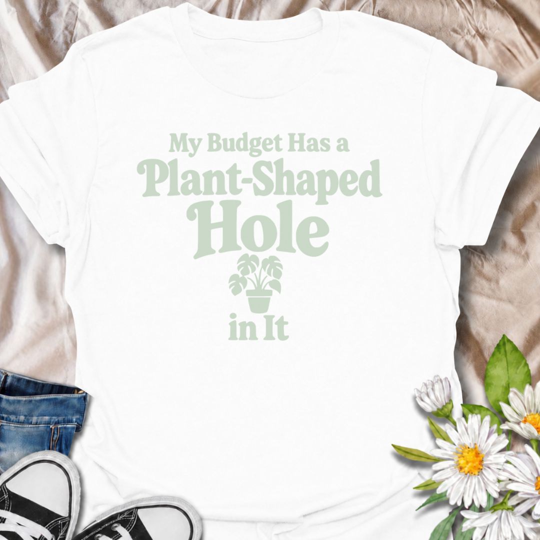 A funny plant T-shirt for anyone whose budget seems to disappear every time a new houseplant comes into view. The phrase “My Budget Has a Plant-Shaped Hole in It” delivers dry, self-aware humor that plant parents and collectors will instantly relate to. Featuring bold retro typography with a small potted plant accent, the design stays clean, readable, and easy to wear. It makes a great gift for nursery regulars, houseplant lovers, and anyone who keeps spending their spare cash on one more plant. Perfect for