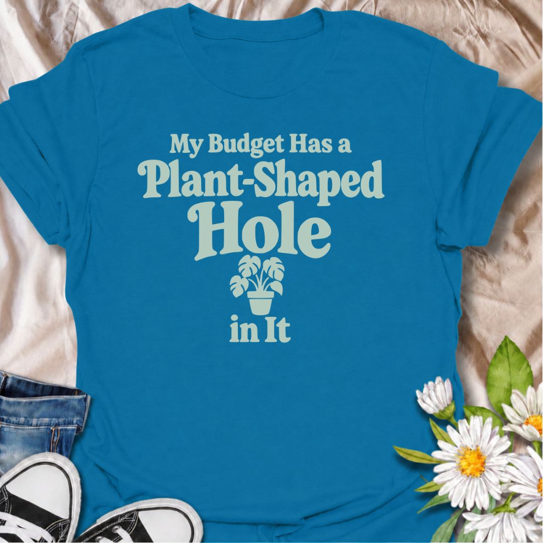 A funny plant T-shirt for anyone whose budget seems to disappear every time a new houseplant comes into view. The phrase “My Budget Has a Plant-Shaped Hole in It” delivers dry, self-aware humor that plant parents and collectors will instantly relate to. Featuring bold retro typography with a small potted plant accent, the design stays clean, readable, and easy to wear. It makes a great gift for nursery regulars, houseplant lovers, and anyone who keeps spending their spare cash on one more plant. Perfect for